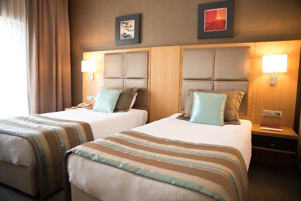 Habitación de hotel con dos camas, cada una con cabecero, lámparas de noche y manta a rayas.