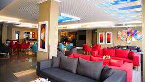A modern hotel lobby with a grey sofa, red and blue chairs, and a ceiling with a sky design. - Efeler Hotel (Aydin)