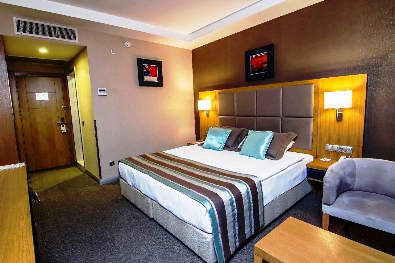Una habitación de hotel con una cama grande, una mesita de noche, una silla y una puerta de madera.