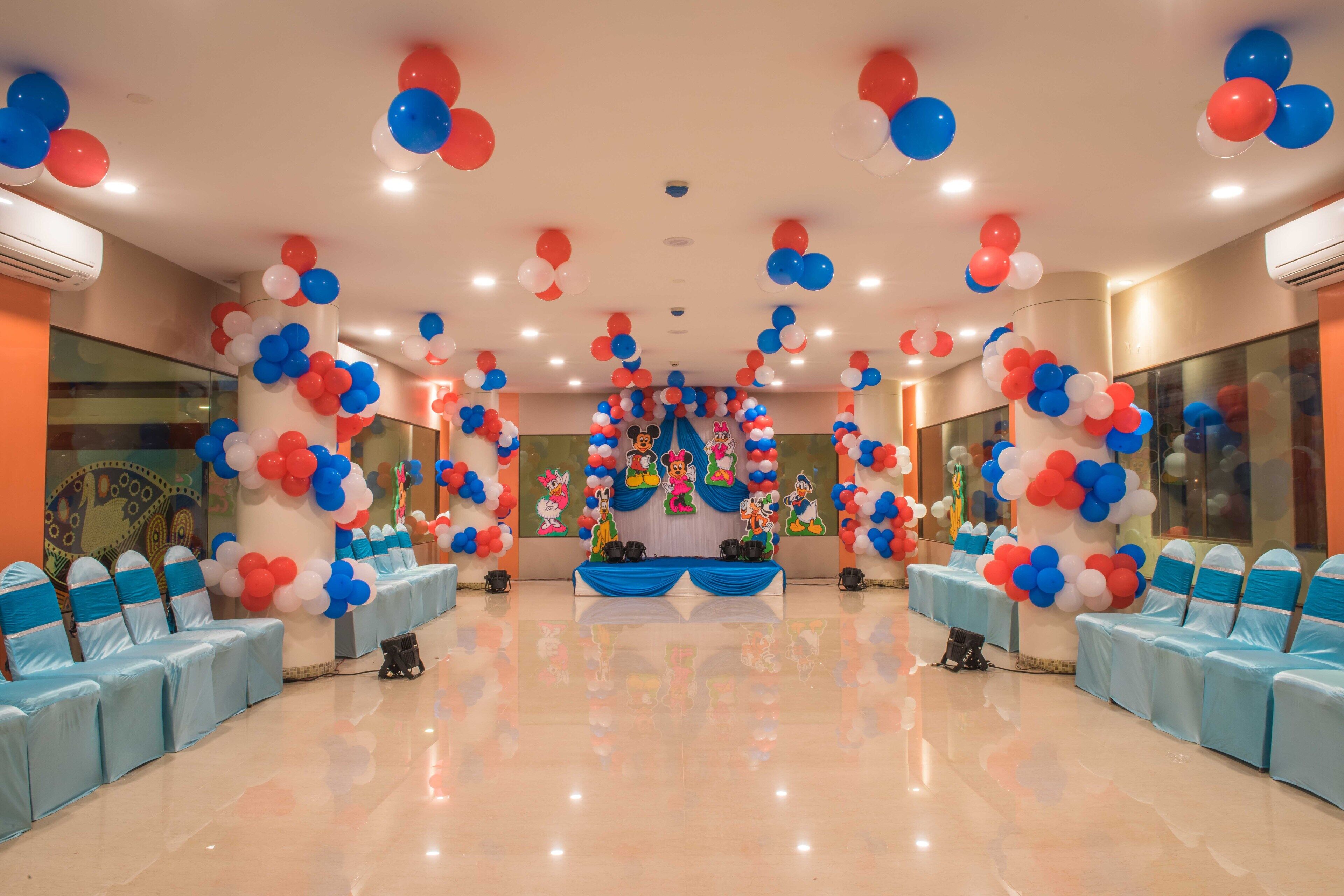 Un salón amplio con filas de sillas azules, un escenario con globos y un gran mural en la pared.
