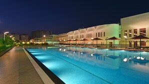 Una piscina con zonas de descanso cercanas, un edificio bien iluminado y un cielo nocturno despejado.