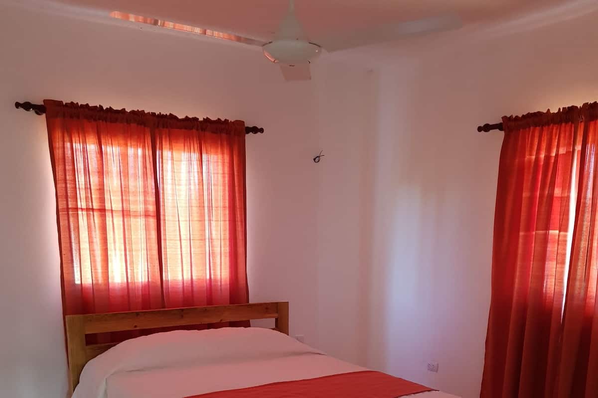 A bedroom with a bed, red curtains, a ceiling fan, and tiled flooring.
