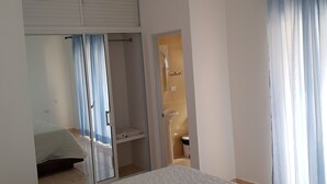 Une chambre à coucher avec un lit, une armoire et une salle de bain visible à travers une porte ouverte.
