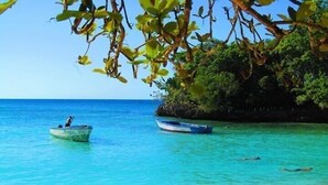 Une plage avec deux bateaux, une eau turquoise et limpide, et un rivage sablonneux.