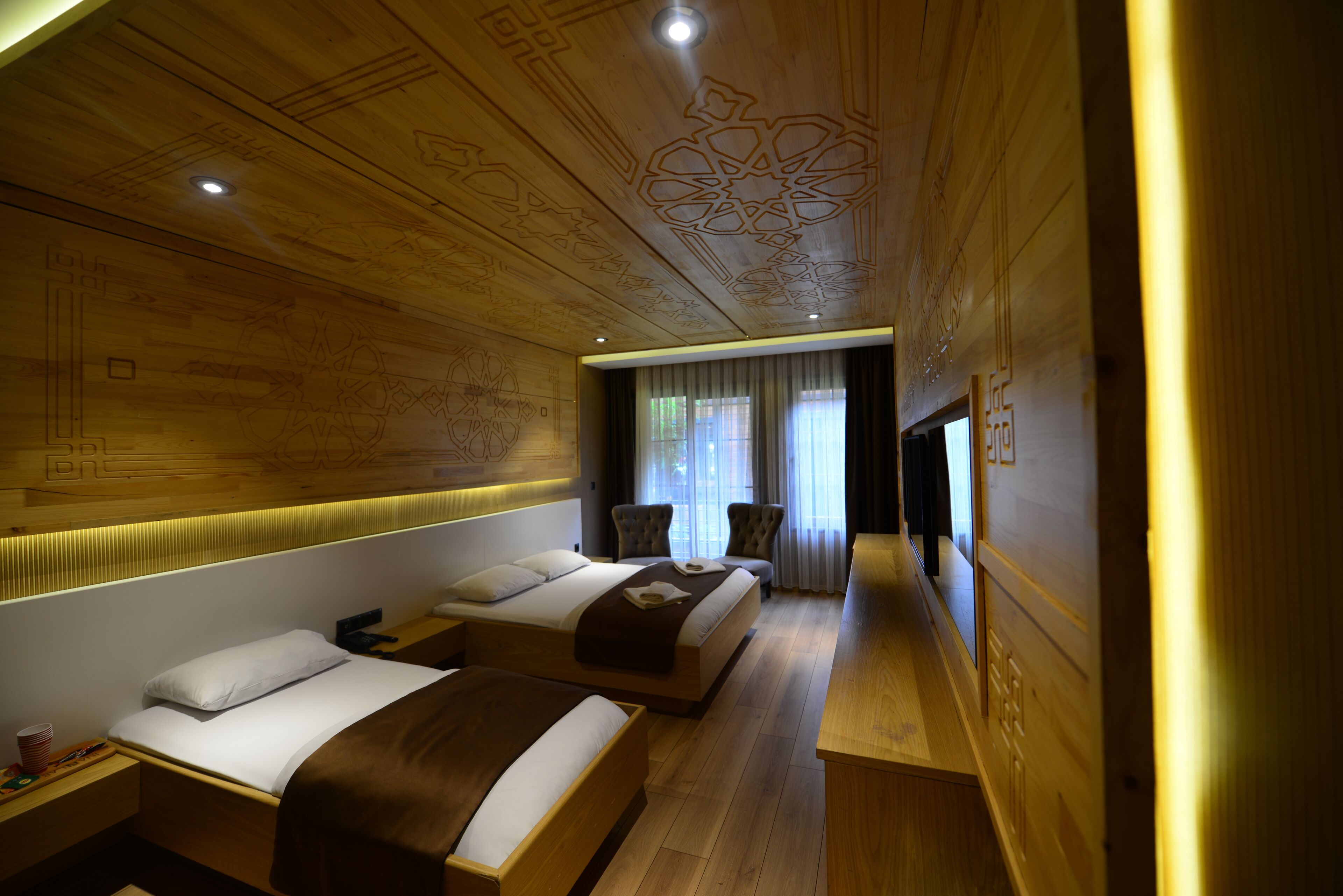 A hotel room with a wooden ceiling, two beds, a desk, and a chair.