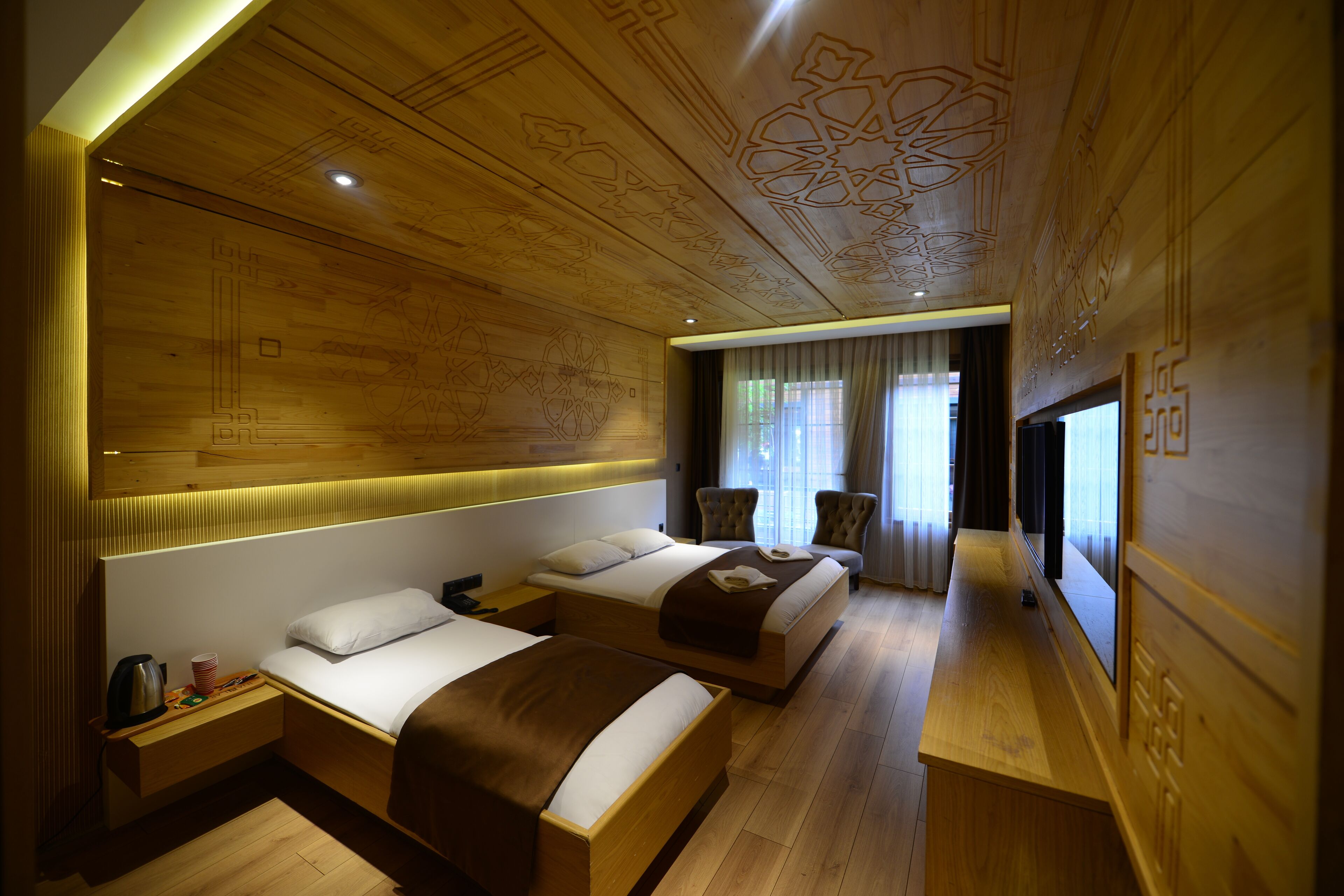 Hotelkamer met twee bedden, een houten plafond met ingewikkelde versieringen, een tafeltje met een waterkoker en een raam met gordijnen.