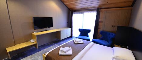 A modern hotel room with a large bed, a flat-screen TV mounted on the wall, a wooden ceiling, and a seating area with a blue chair.