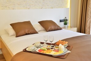 Ein ordentlich bezogenes Bett mit braunen Kissen, ein Frühstückstablett mit Eiern, Brot und Obst sowie zwei Weingläsern.