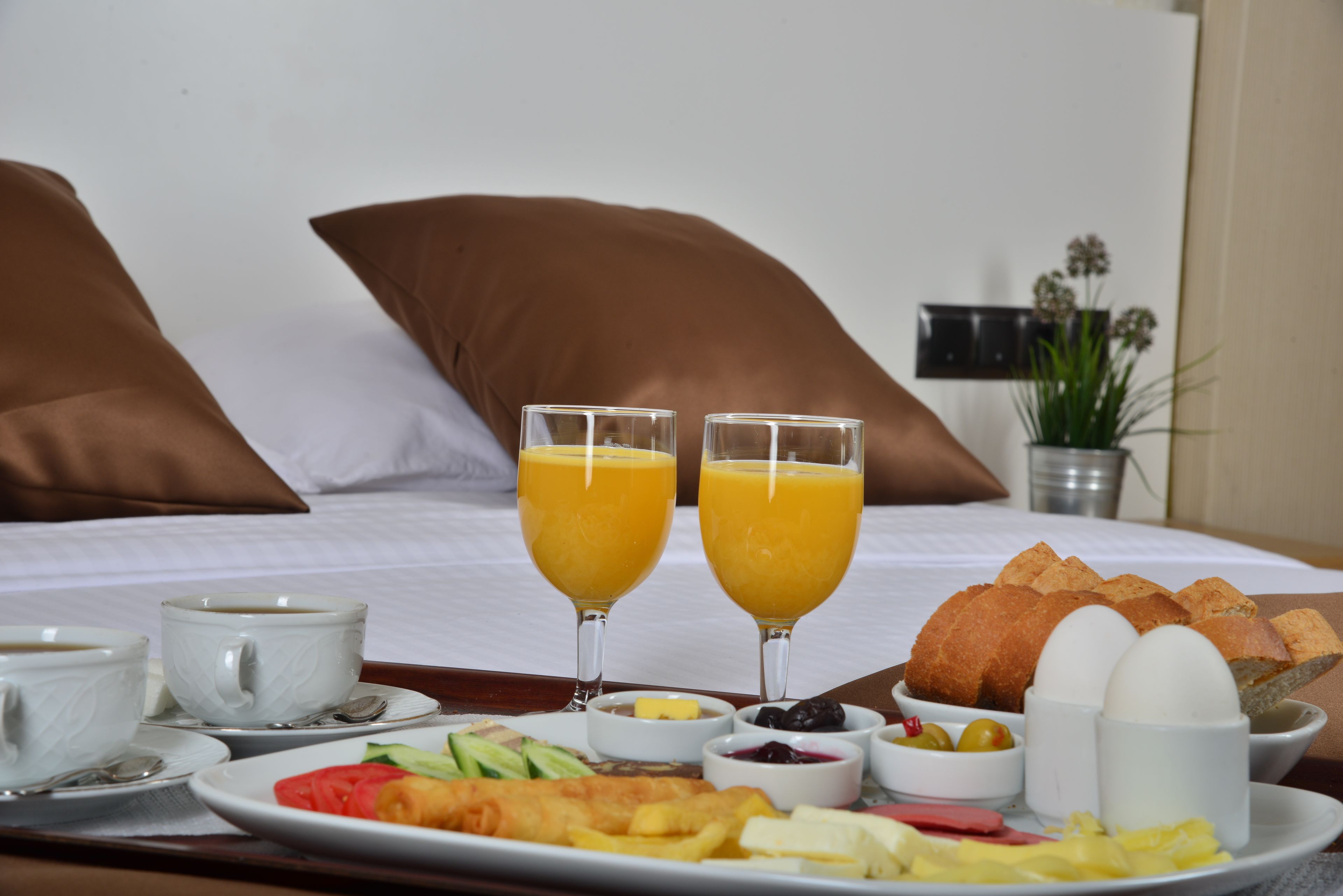 Bandeja de desayuno con croissants, huevos y fruta sobre una cama con almohadas.