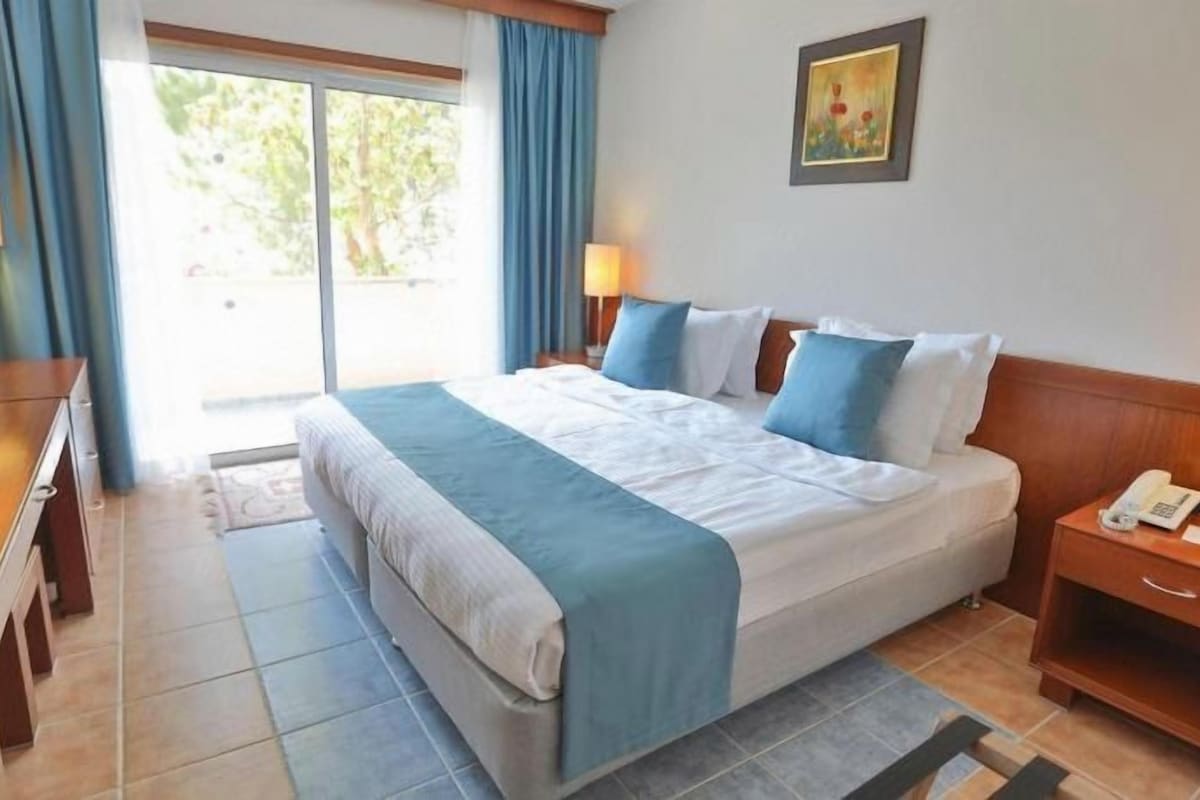 A hotel room with a bed, bedside tables, a desk, and a view of the outdoors.