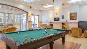 A pool table with balls, wicker chairs, and a television in a well-lit room with a large window and a door leading outside. - Happy Hotel Kalkan (Kas)
