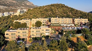 A hillside hotel with multiple buildings, a pool area, and a mountainous backdrop. - Happy Hotel Kalkan (Kas)