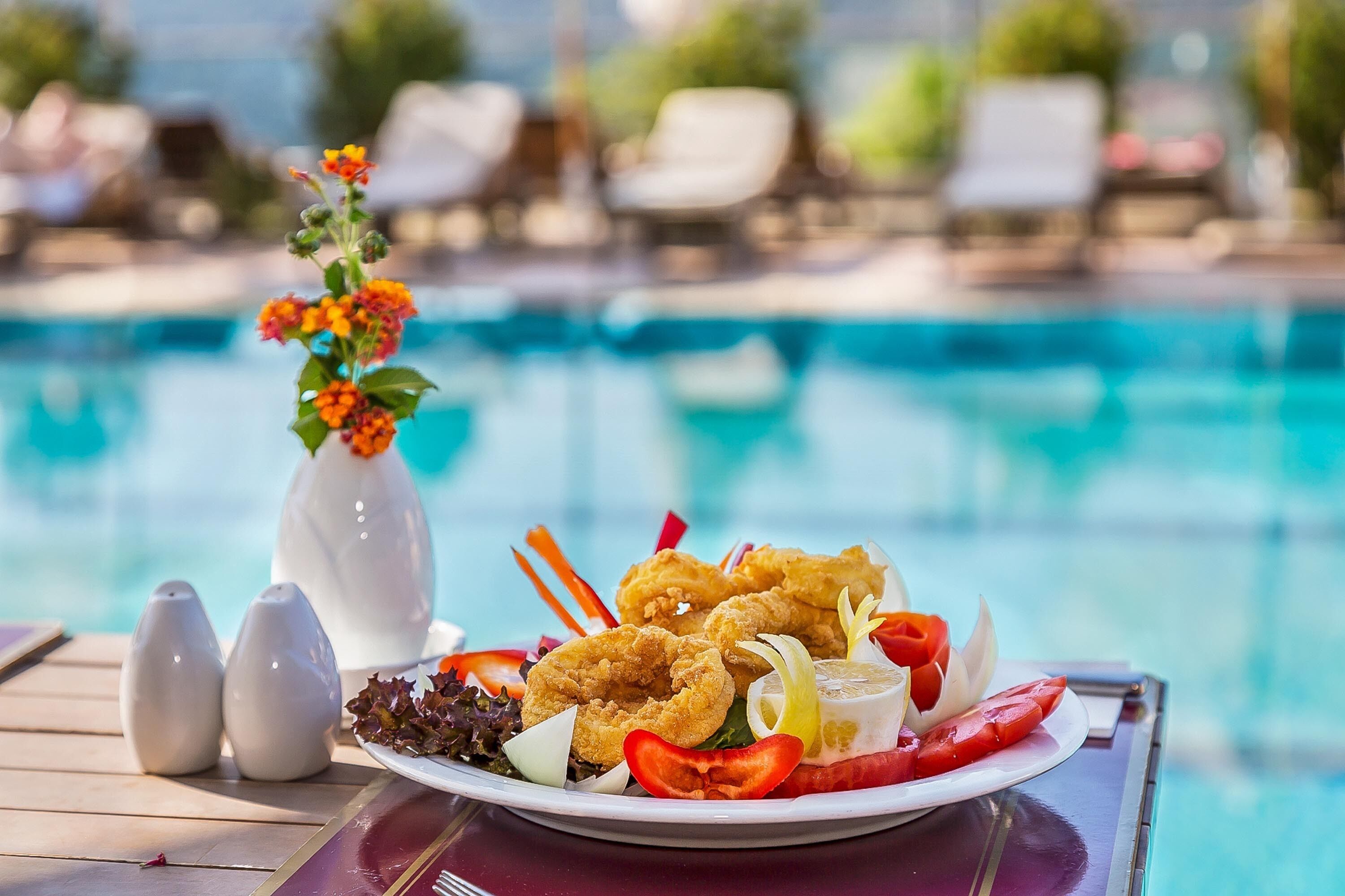 Plato de comida con camarones, ensalada y verduras junto a una mesa al lado de la piscina.