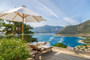Un balcon doté d’une terrasse en bois, de chaises longues et d’un grand parasol.