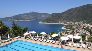 A poolside area with lounge chairs and umbrellas, overlooking a coastal town and a clear blue sea. - Happy Hotel Kalkan (Kas)