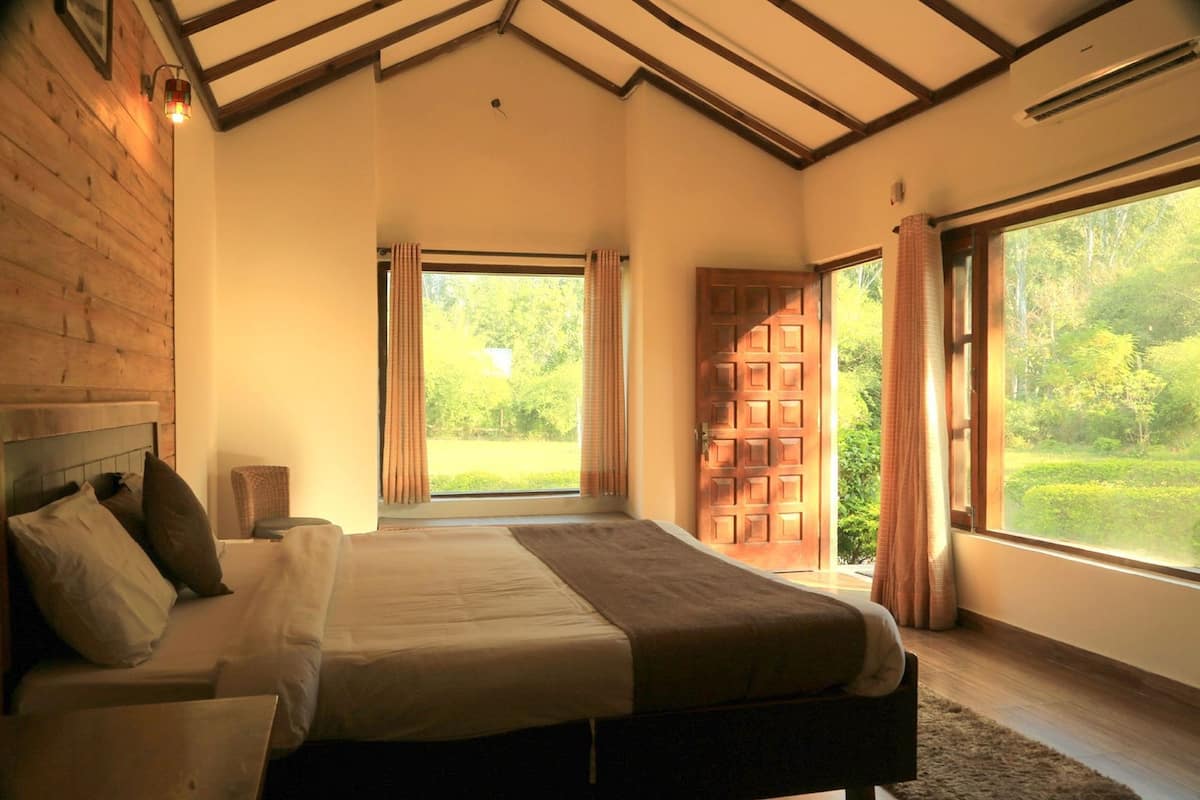 A bedroom with a large bed, a wooden headboard, a nightstand, and a window with curtains.