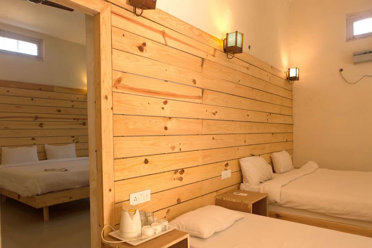 A room with wooden panel walls, two beds, bedside tables, and a wall-mounted heater.