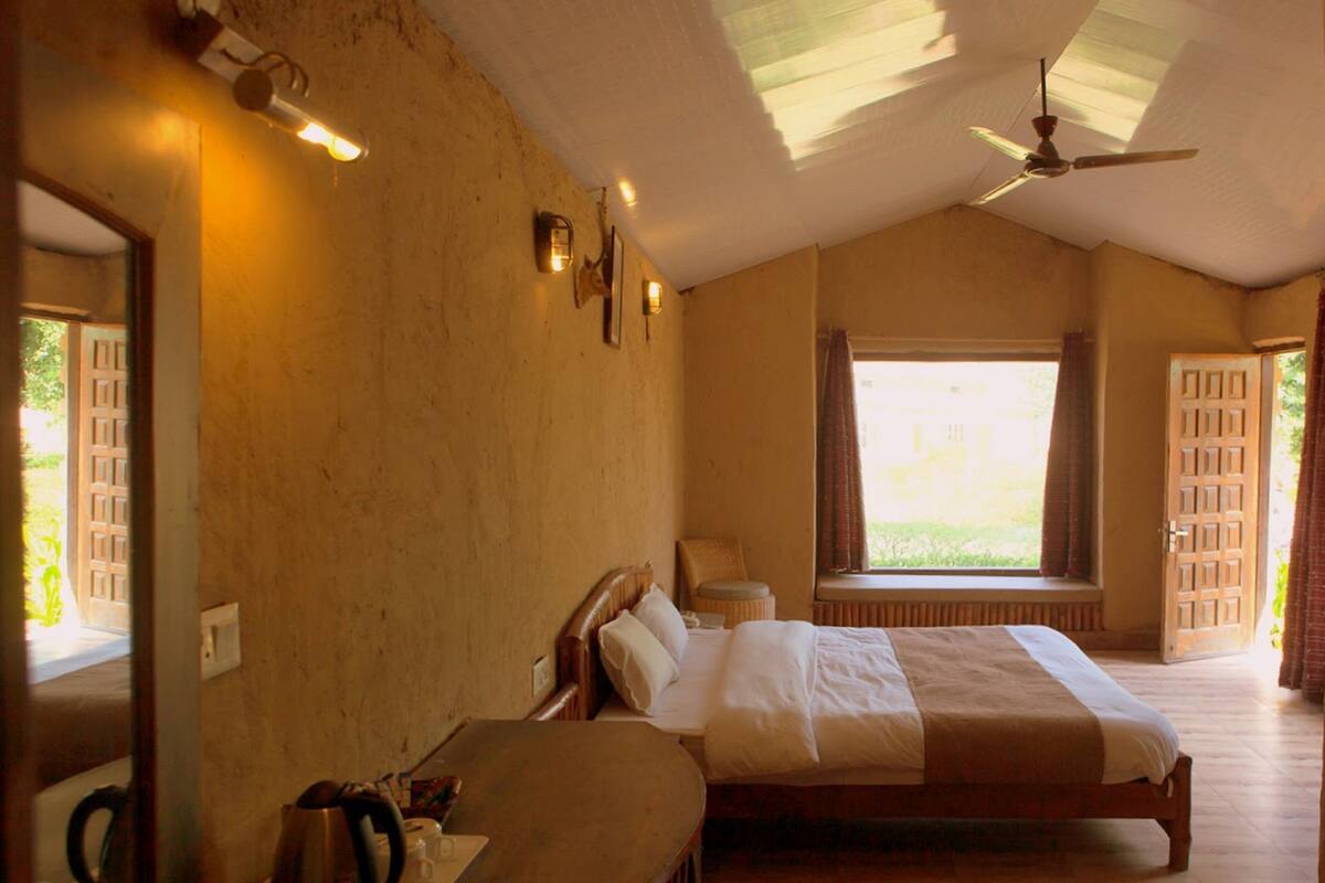 A bedroom with a large bed, a wooden desk, a ceiling fan, and a window with curtains.