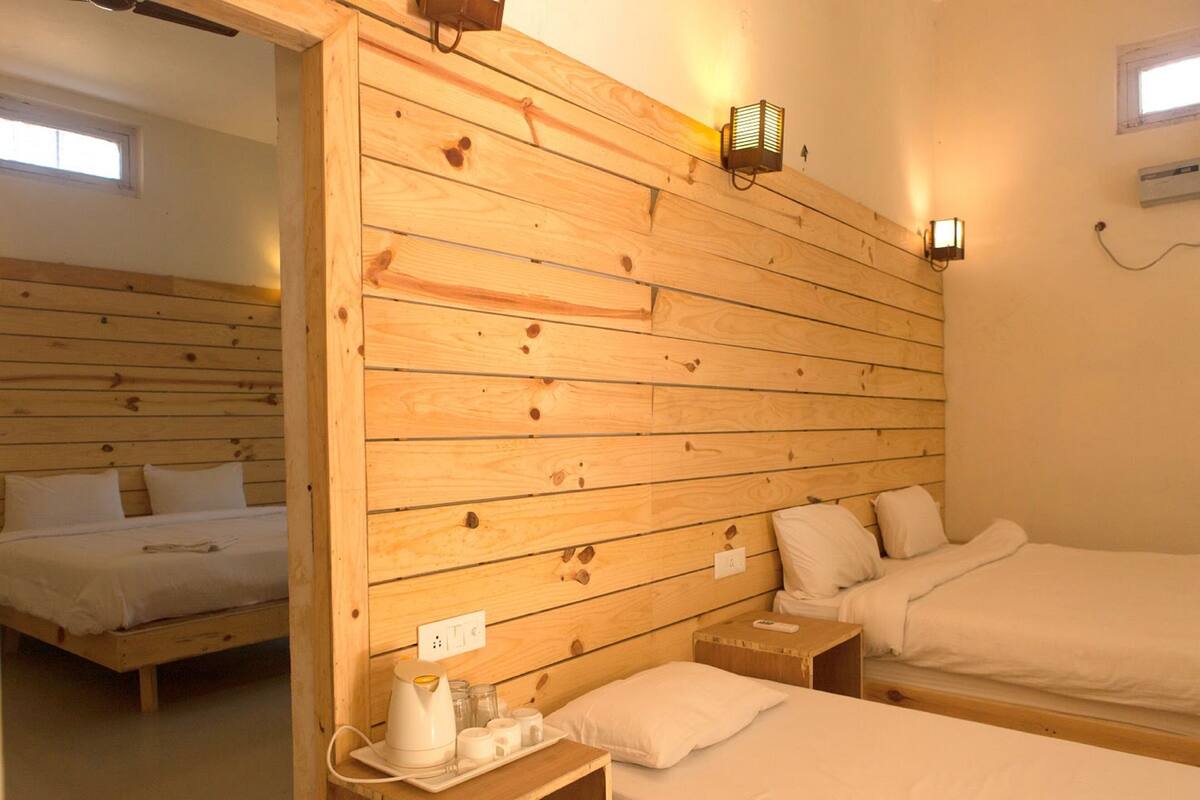 A room with wooden panel walls, two beds, bedside tables, a heater, and wall-mounted lights.