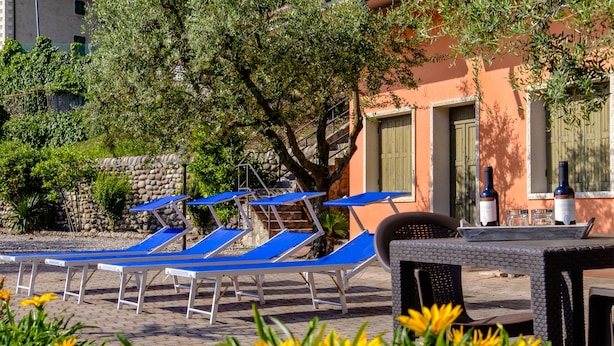 A poolside area with blue lounge chairs, a stone wall, and a building with green shutters. - Agriturismo Al Colle (Cavaion Veronese)