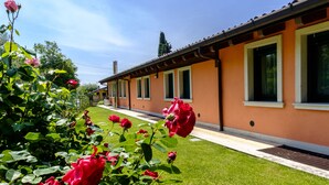 A row of orange buildings with green lawns and red roses in the foreground. - Agriturismo Al Colle (Cavaion Veronese)