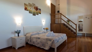 A bedroom with a wooden floor, a bed with a quilt, a nightstand with a vase, and a staircase. - Agriturismo Al Colle (Cavaion Veronese)