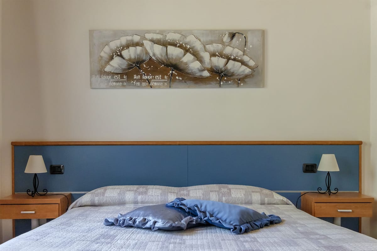 A bedroom with a bed, two bedside tables with lamps, and a wall-mounted artwork.