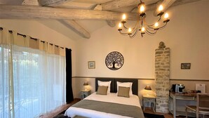 A hotel room with a large bed, a chandelier, a stone wall, and a desk with a computer. - Le Mas Carré (Seguret)