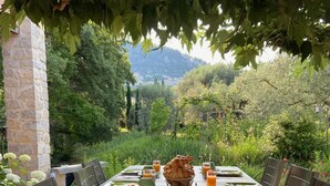 An outdoor dining table set with plates, glasses, and a basket of bread, surrounded by chairs and greenery. - Le Mas Carré (Seguret)