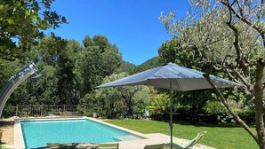 A swimming pool with a stone wall, a lounge chair, and a large umbrella. - Le Mas Carré (Seguret)