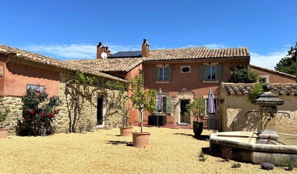 A courtyard with stone buildings, a fountain, and potted plants. - Le Mas Carré (Seguret)