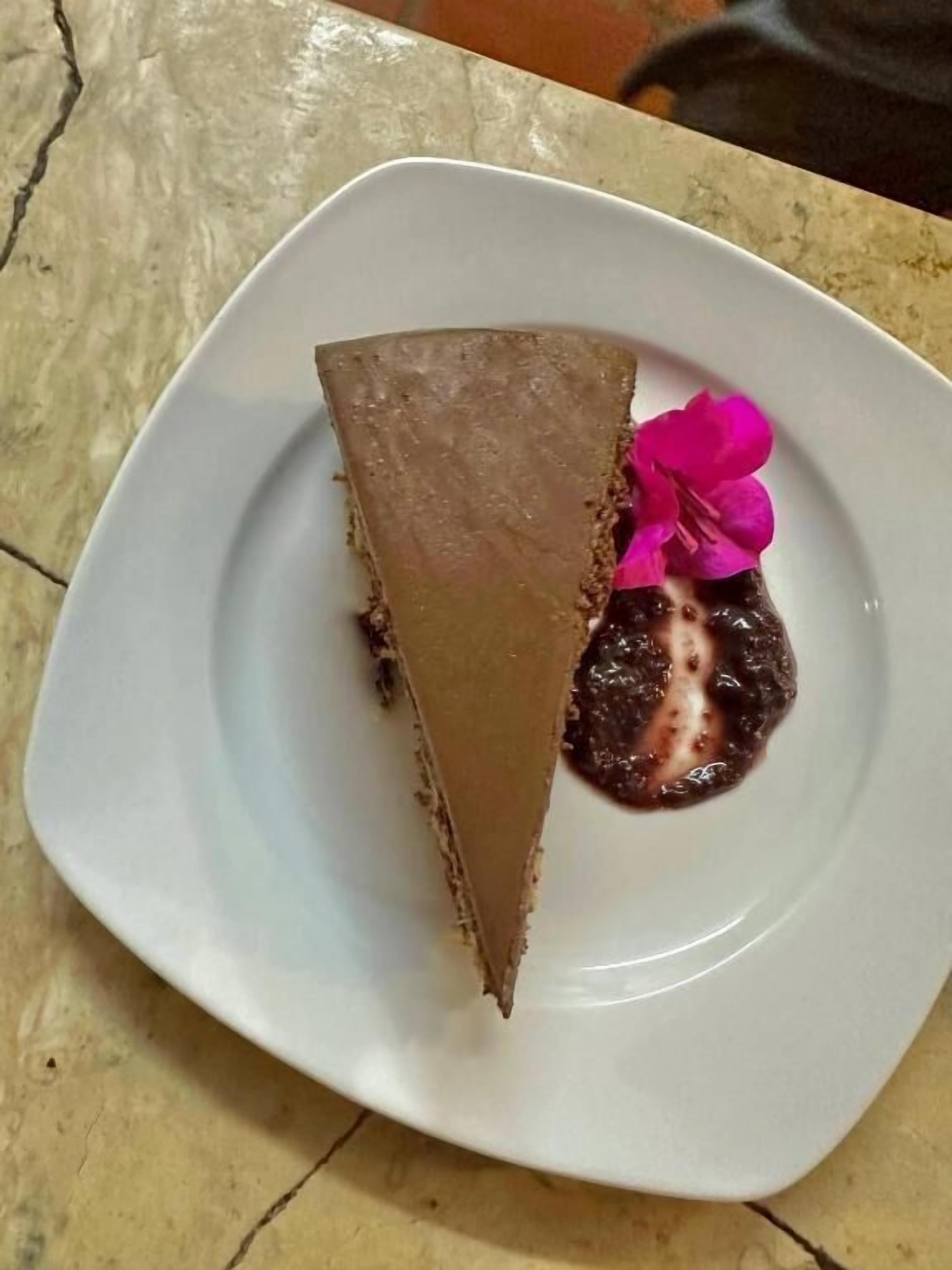 A slice of chocolate cake on a white plate with a pink flower decoration.