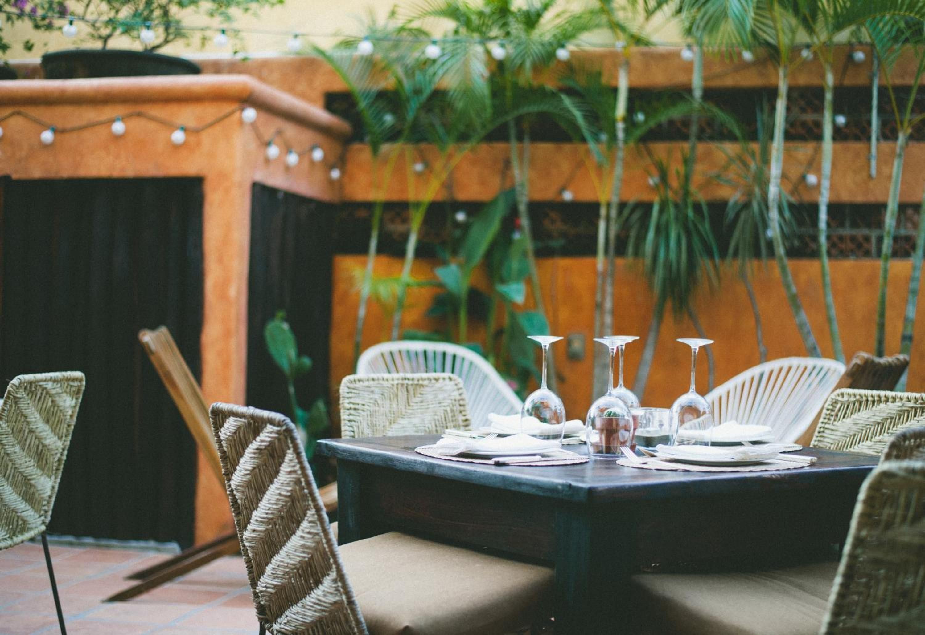 Un área de comedor al aire libre con sillas de mimbre, una mesa dispuesta con platos, vasos y cubiertos.