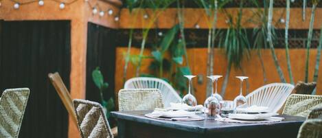 An outdoor dining area with wicker chairs, a table set with plates, glasses, and cutlery.