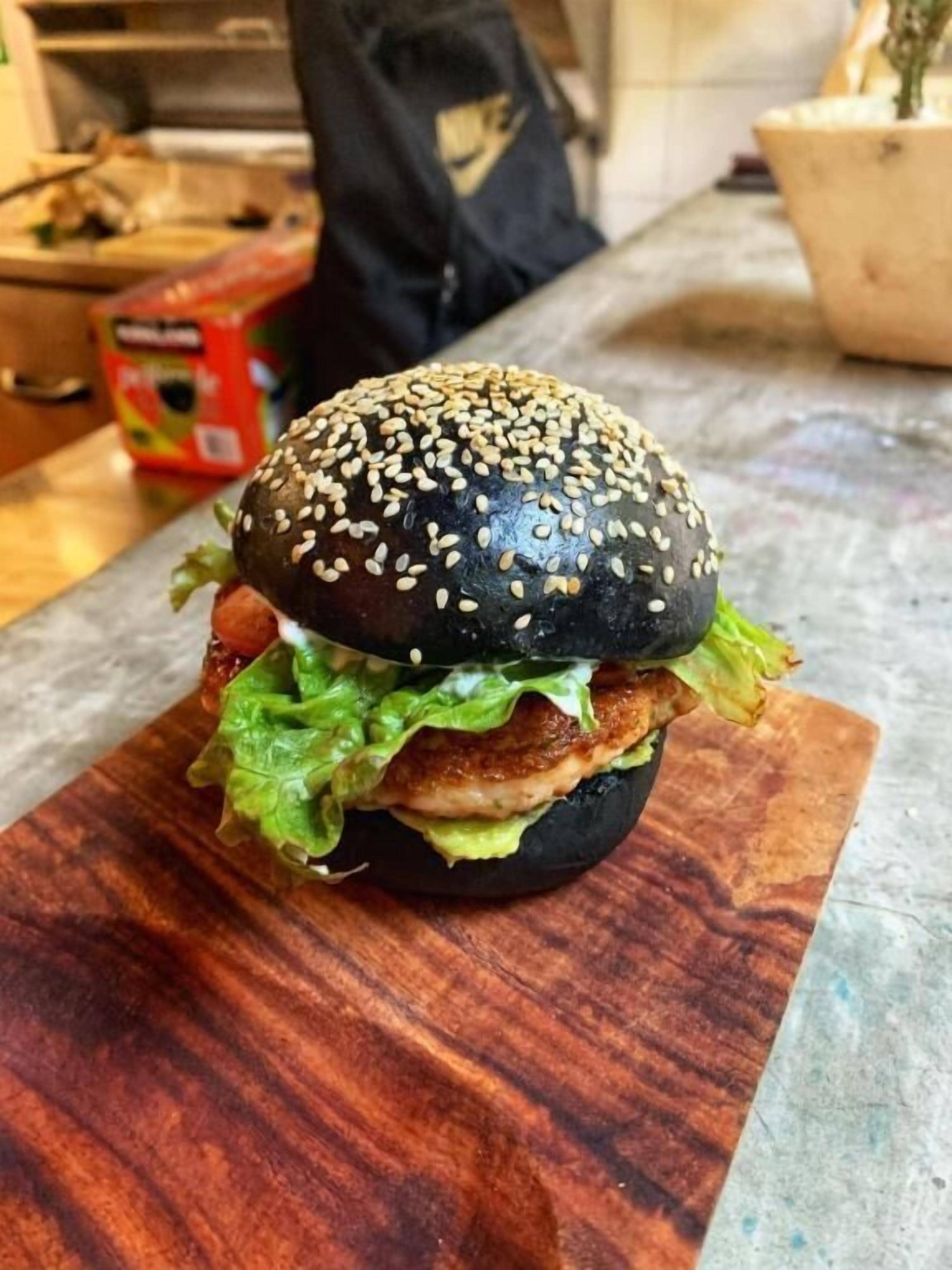 A burger with sesame seed bun on a wooden cutting board.