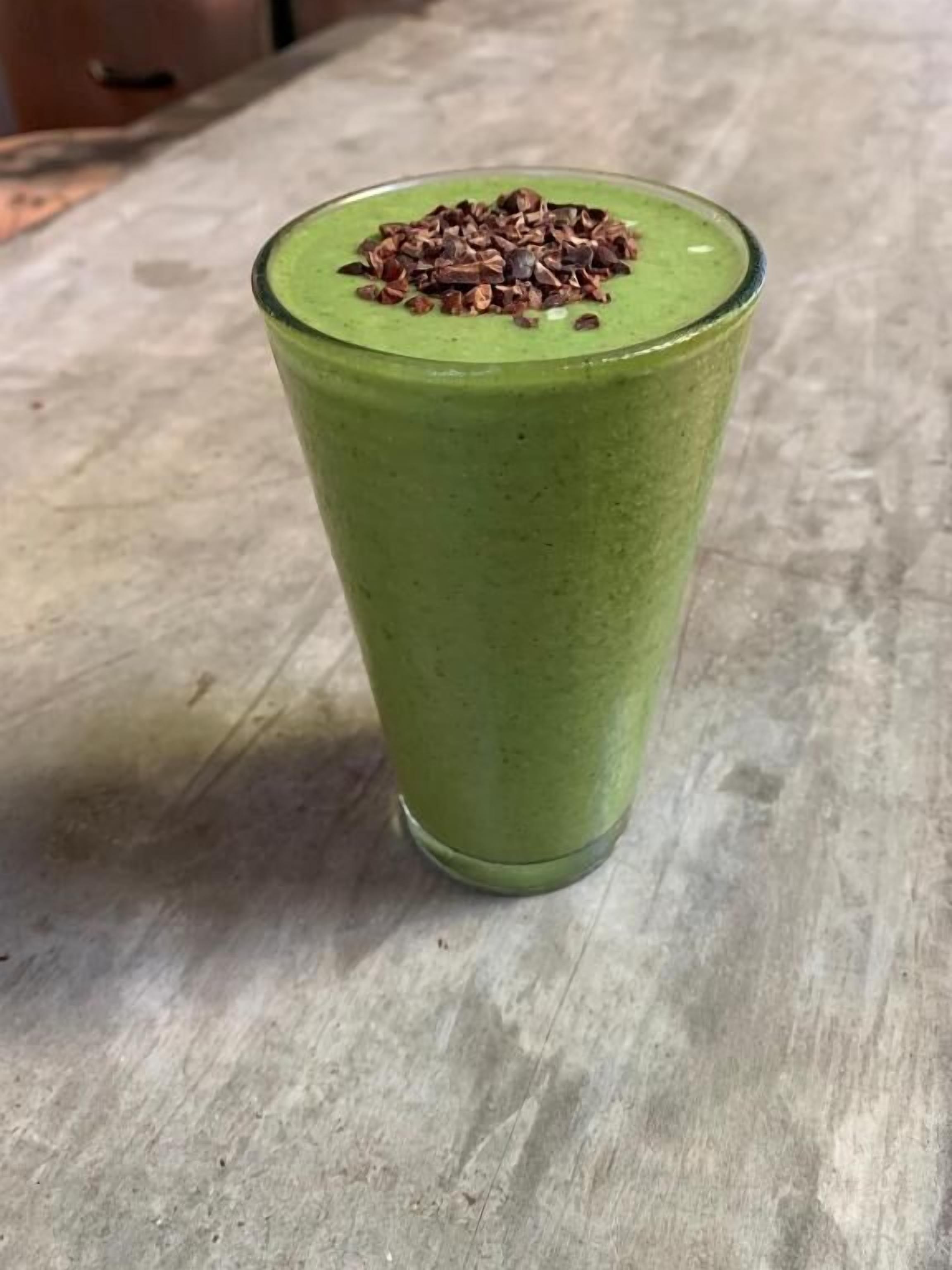 A tall glass of green smoothie on a textured surface.