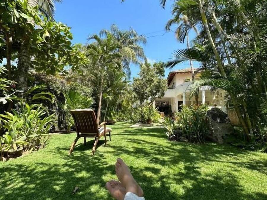 Una persona recostada en una silla de descanso en un área verde, con vista a un edificio y palmeras.