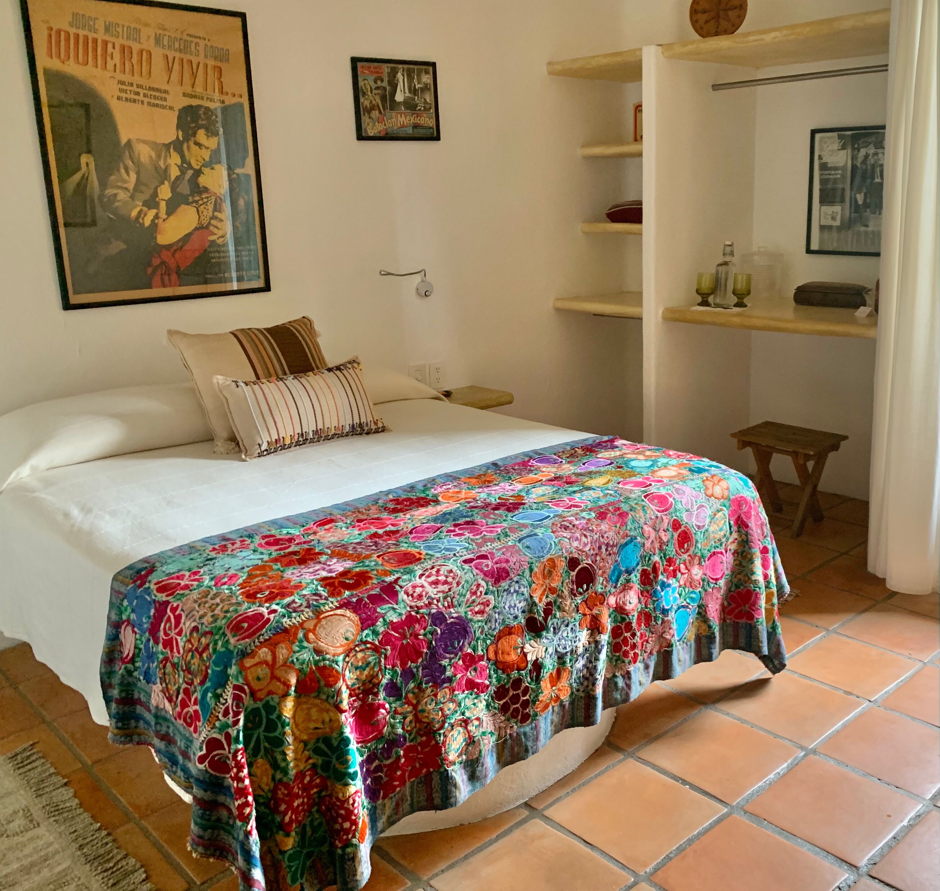 A bedroom with a bed, a colorful quilt, a shelf with items, and a poster on the wall.