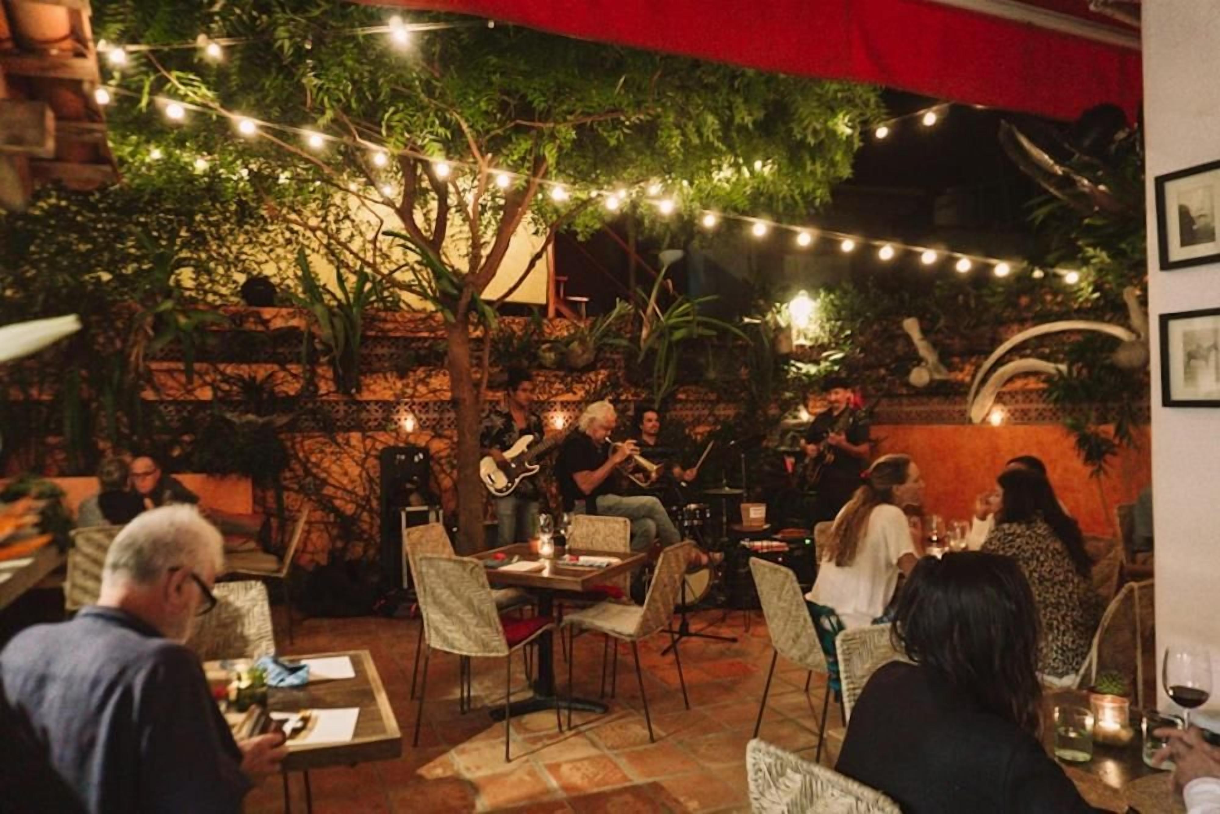 An outdoor dining area with string lights, tables, chairs, and a band performing.