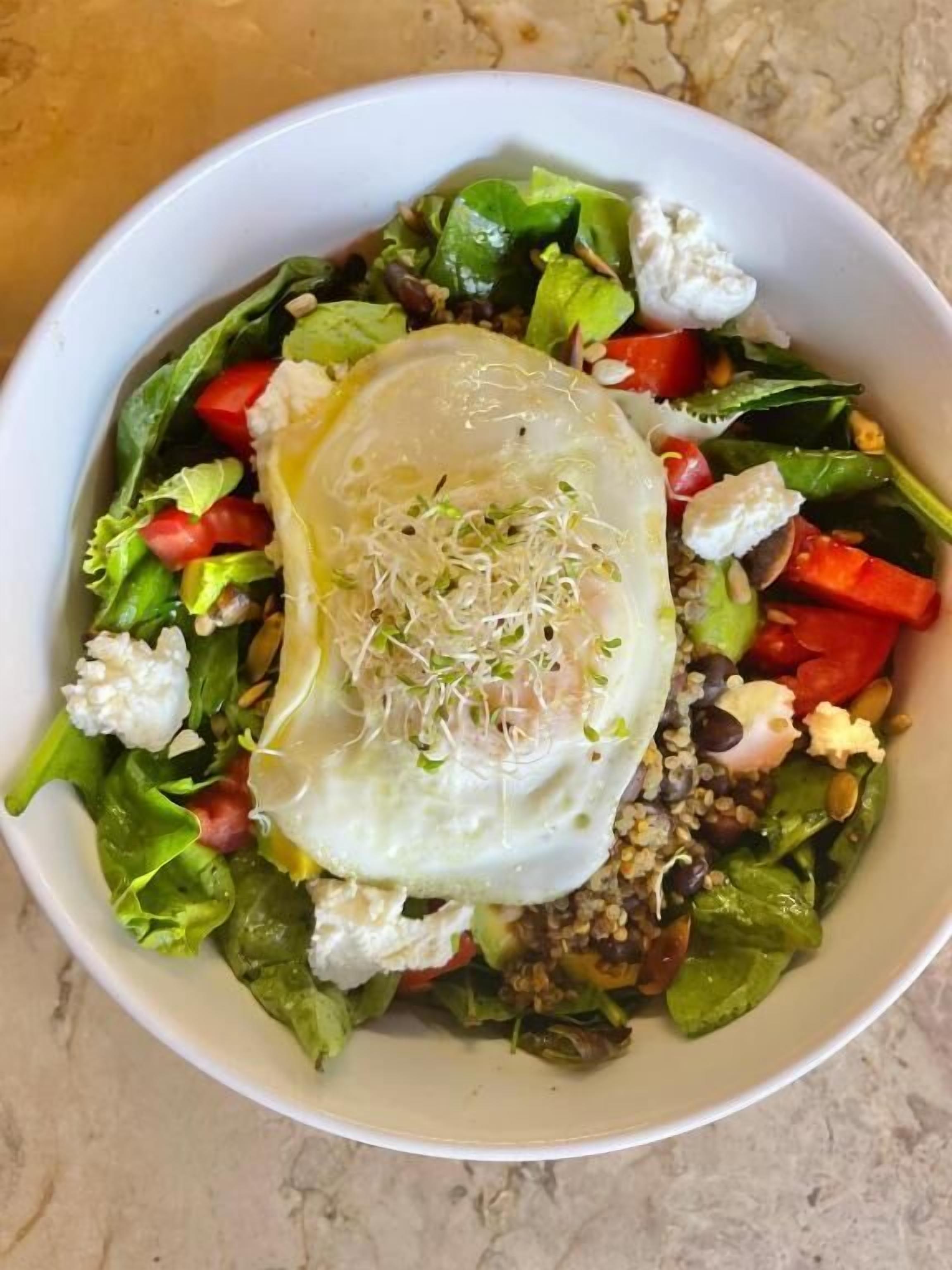 A bowl of salad with a poached egg on top, containing various vegetables and grains.