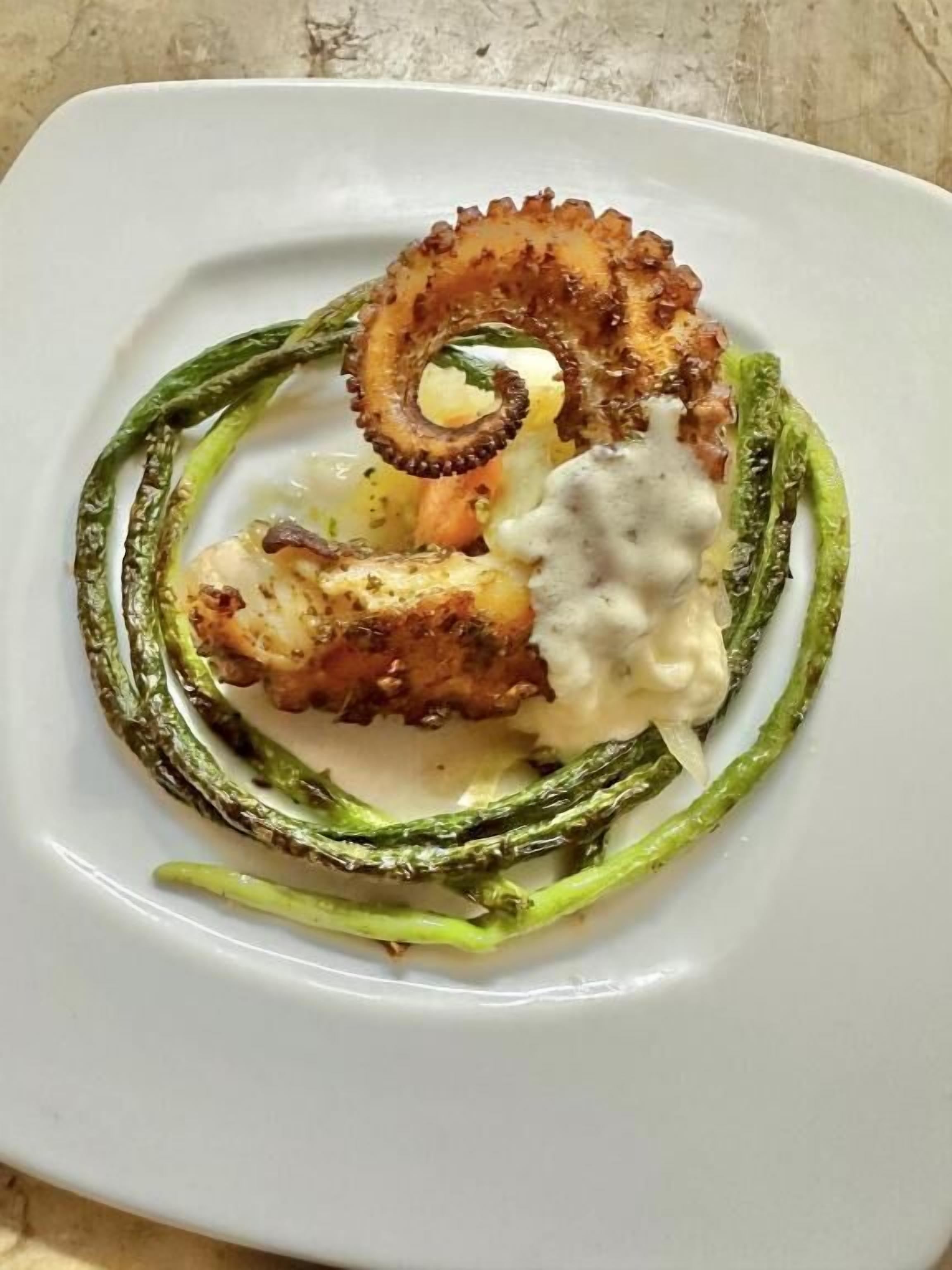 A plate with grilled octopus, asparagus, and a creamy sauce.