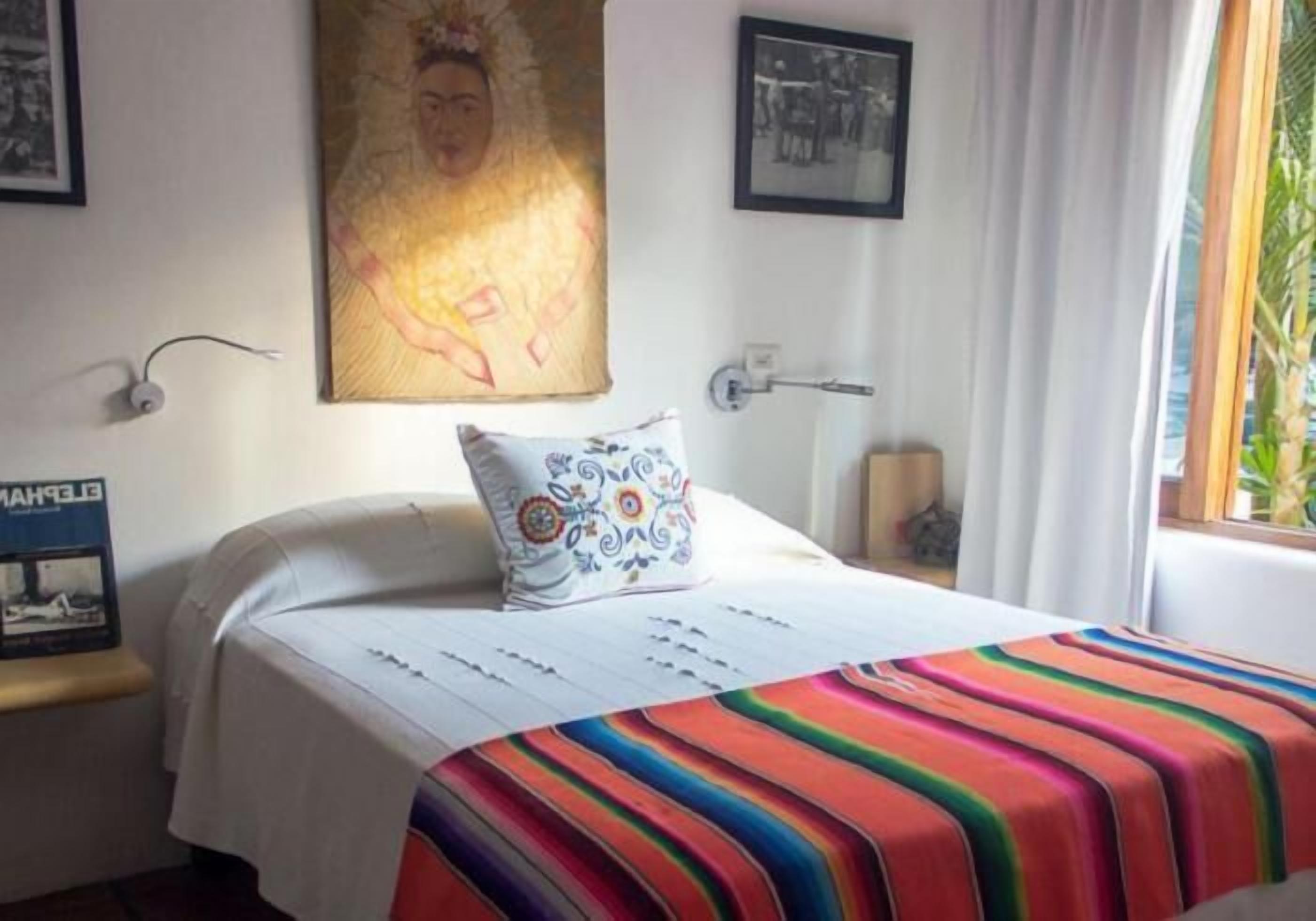 A bed with a colorful striped blanket, a decorative pillow, and a wall with a framed picture.