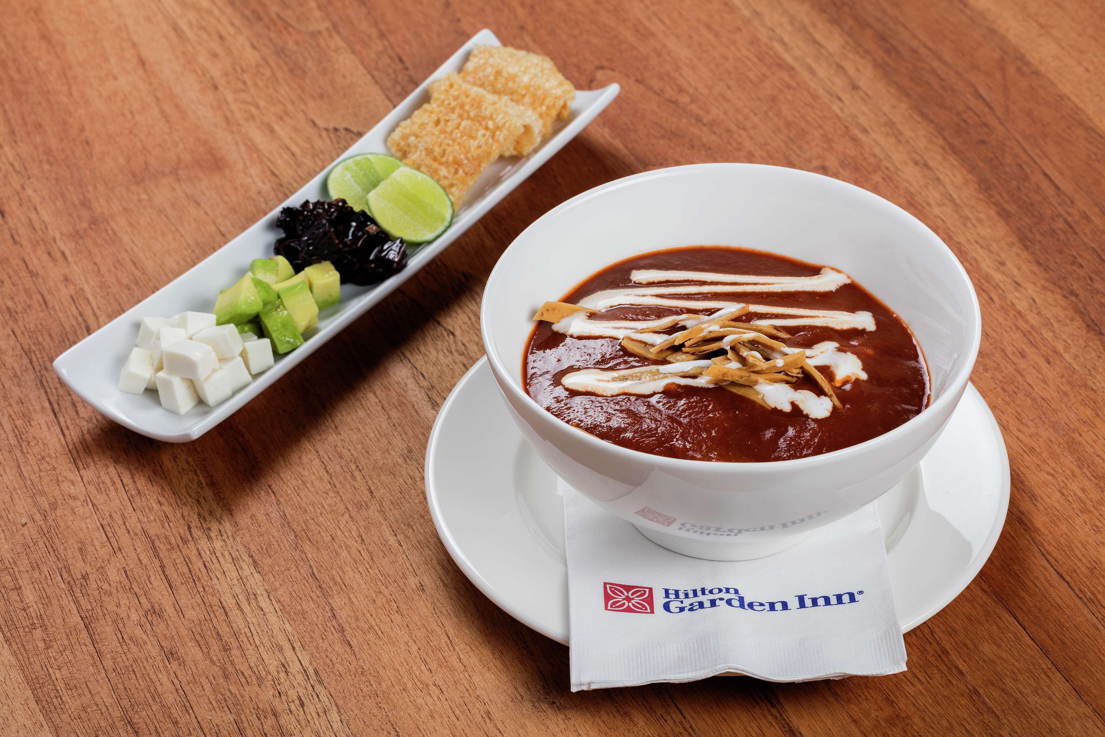 A bowl of soup with toppings, a side dish with lime and avocado, and a napkin with the Hilton Garden Inn logo.