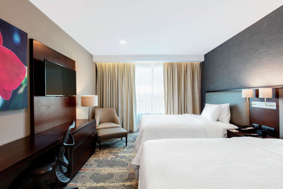 Habitación de hotel con dos camas, un escritorio, una silla, un televisor y una ventana con cortinas.
