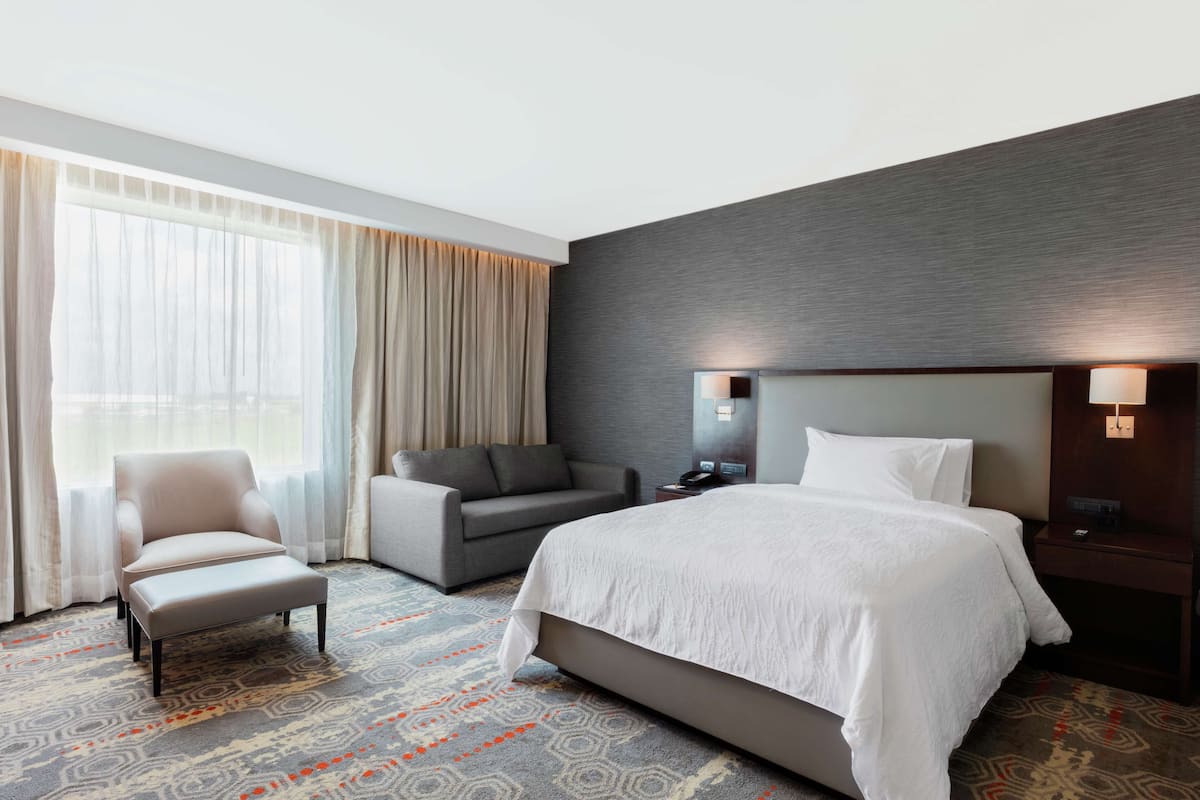 Una habitación de hotel con una cama grande, una silla, un sofá y un escritorio con lámpara.