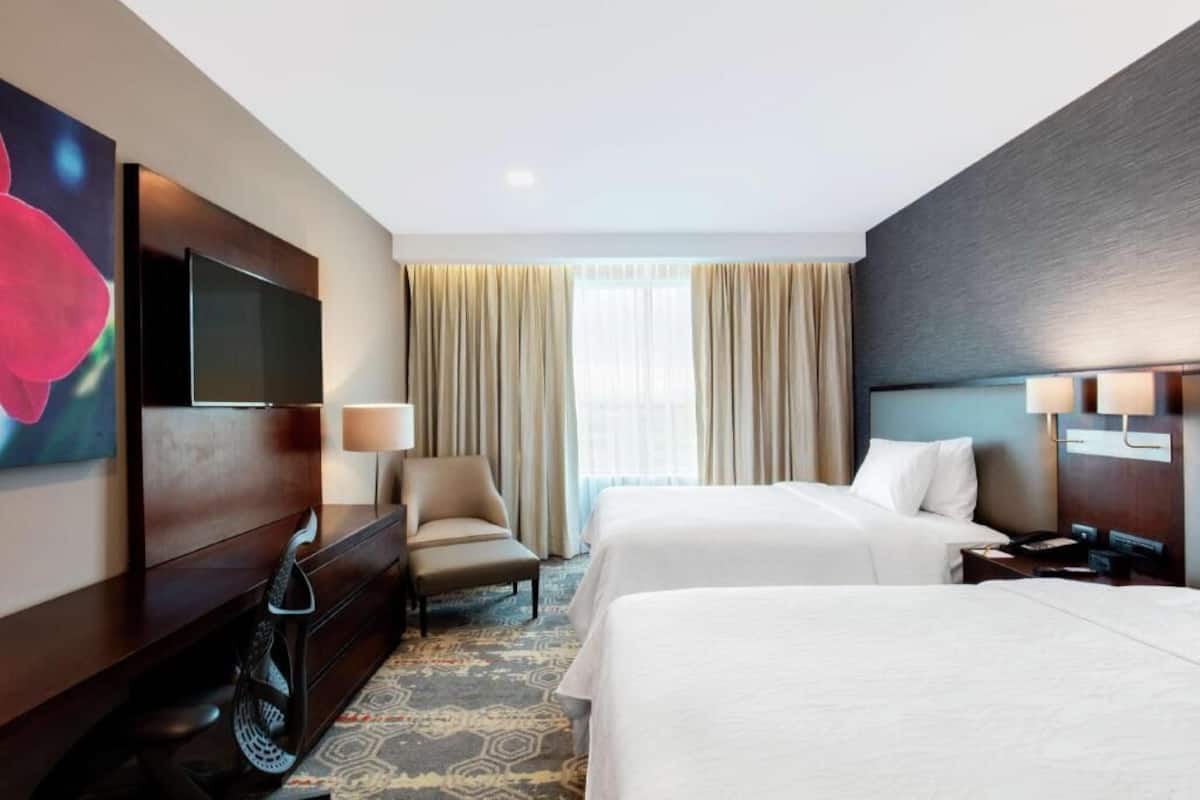 Habitación de hotel con dos camas, televisión, escritorio, silla y ventana con cortinas.