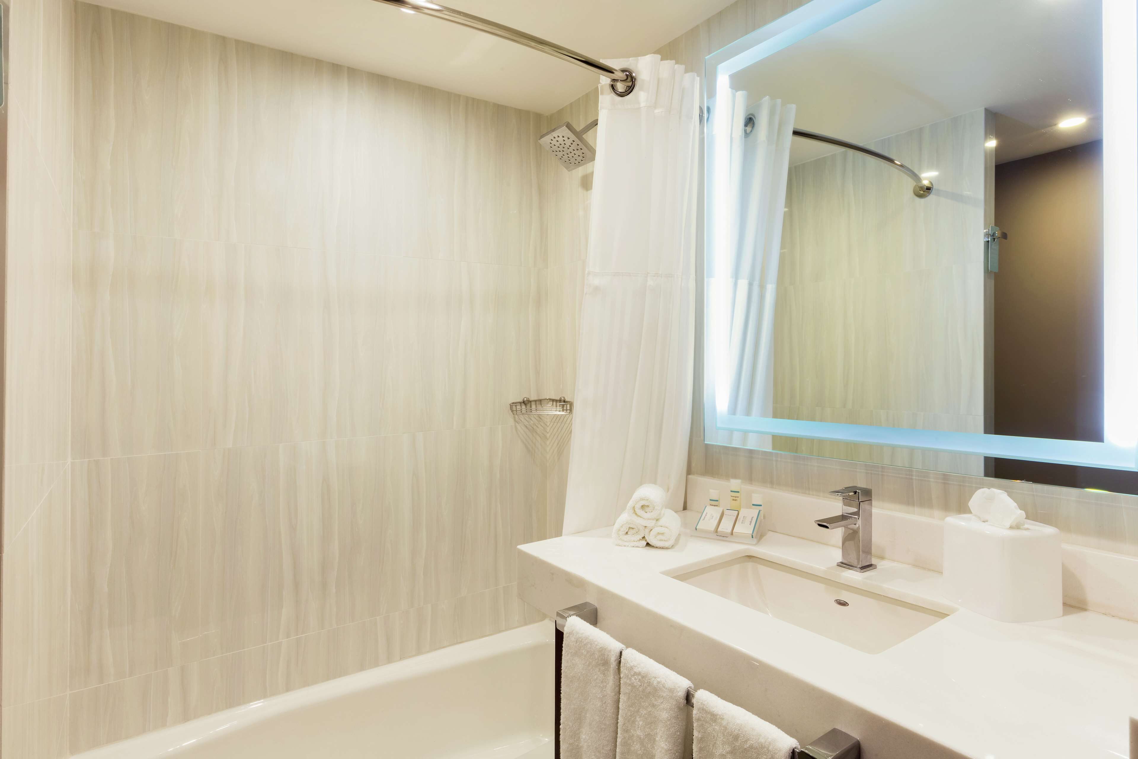 Et moderne badeværelse med badekar, vask med toiletartikler og bruser med bruseforhæng.