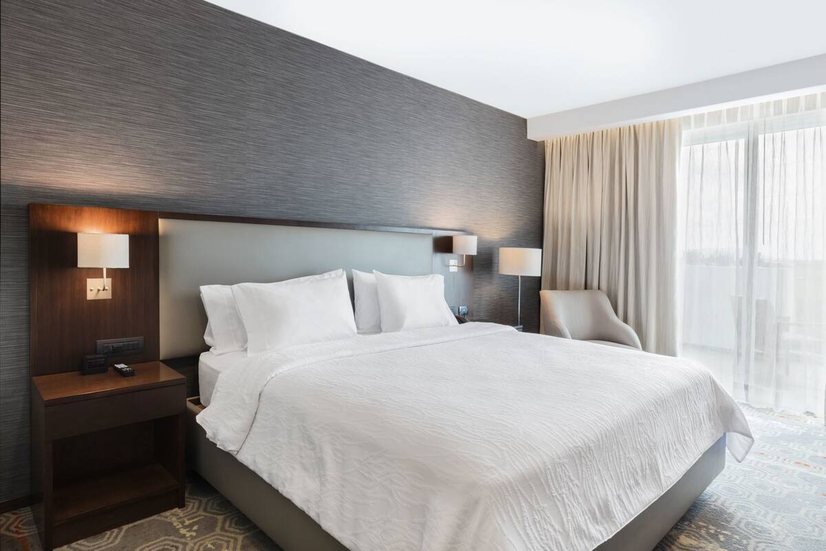 Habitación de hotel con una cama grande, dos mesitas de noche, un cabecero y vistas al exterior.