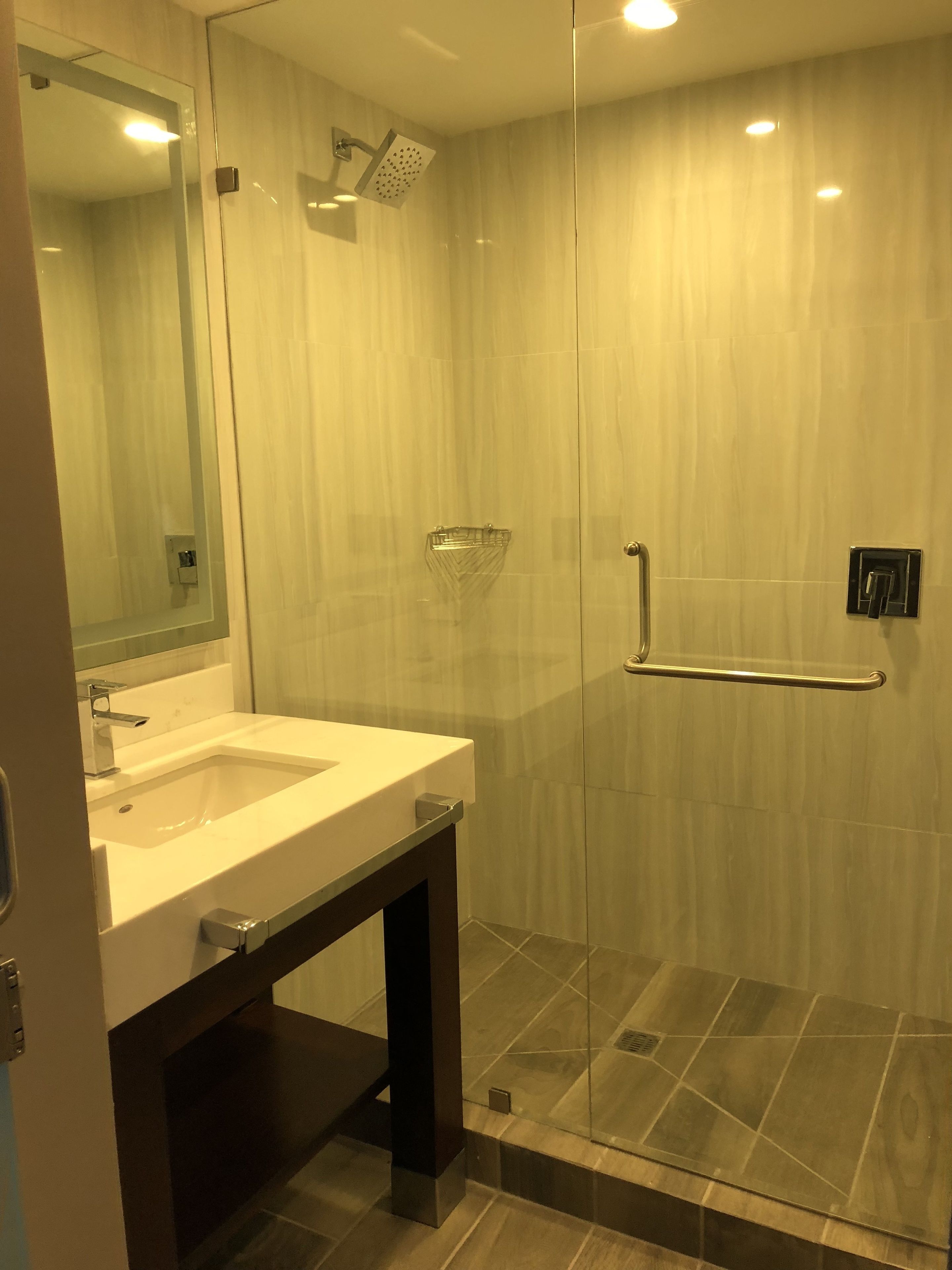 A modern bathroom with a glass shower enclosure, a vanity with a sink, and a mirror.