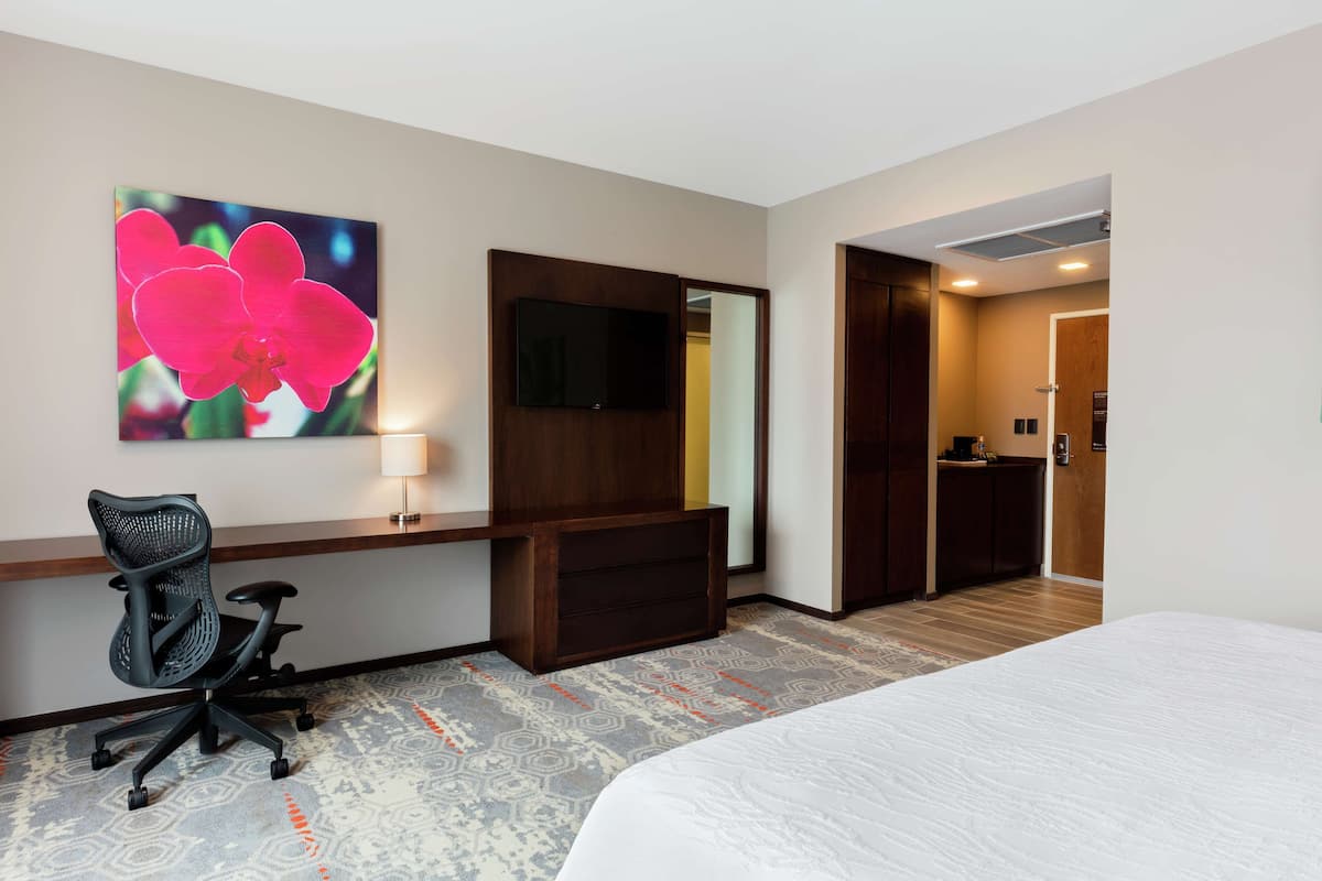 Una habitación de hotel con cama, un escritorio con silla, un televisor fijado a la pared y un baño visible a través de una puerta abierta.